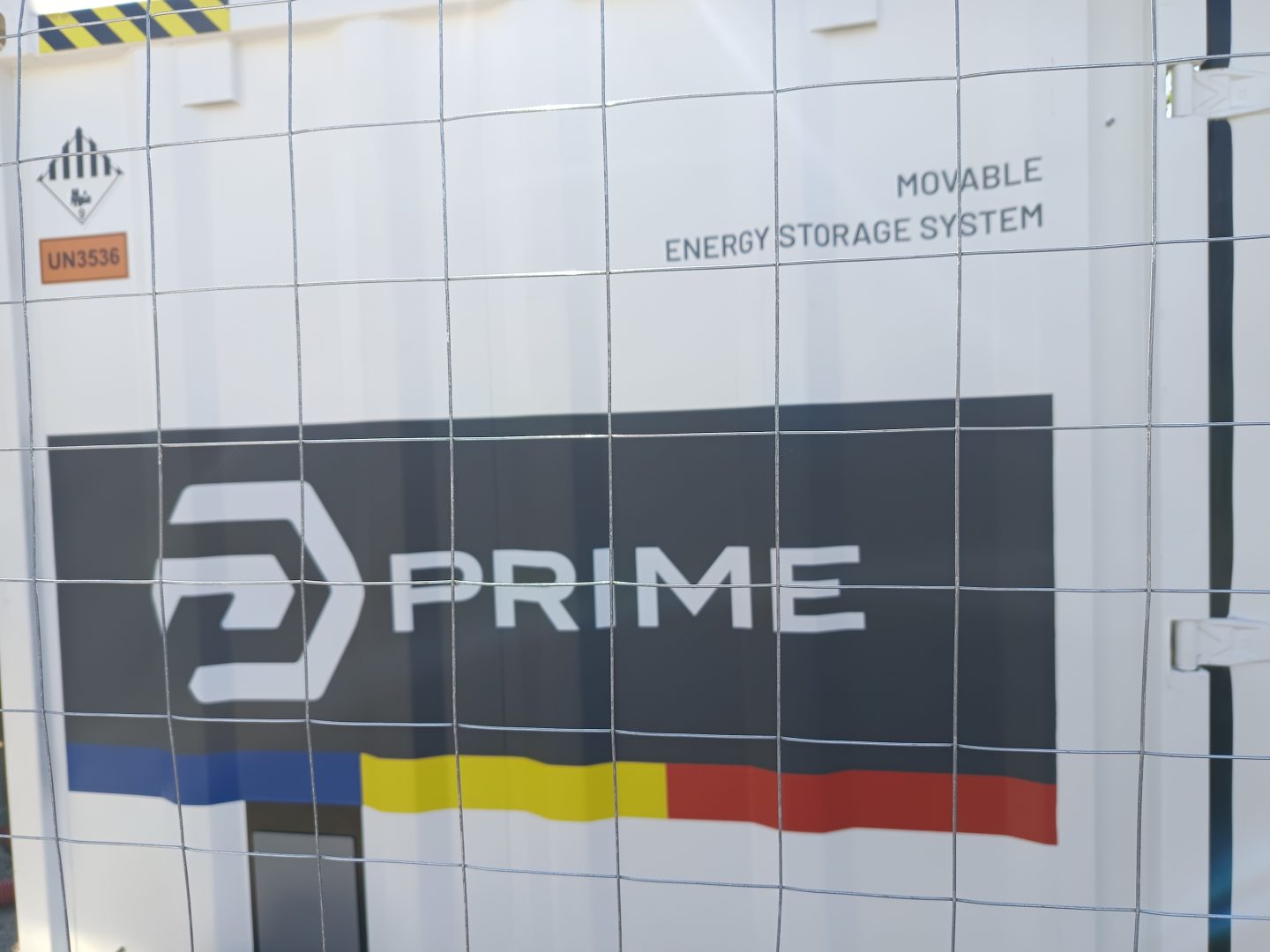 Container exterior PRIME Movable Energy Storage System in spatele unui gard metalic